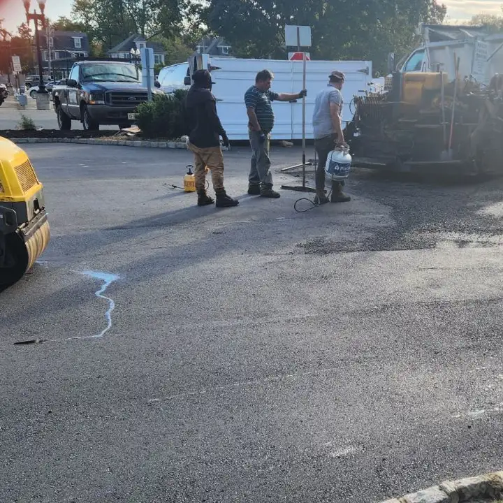 Three construction workers paving a parking lot with a road roller nearby.